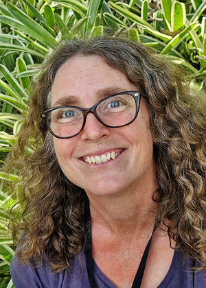 Person with curly hair standing in front of green foliage