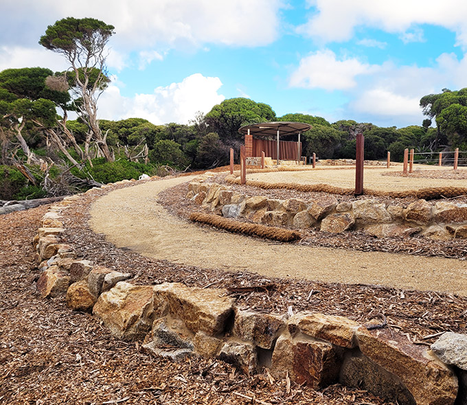 A winding path bordered by irregularly shaped stones leads through lush greenery and trees.