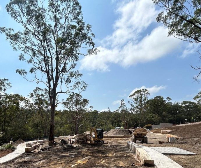 A cleared area overlooking a thickly treed landscape of eucalypts with small construction machinery in the foreground