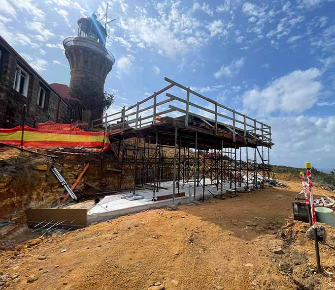 A construction site with scaffolding next to an old lighthouse under a clear sky