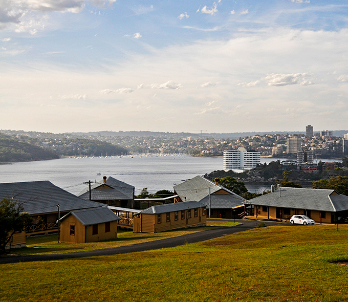 A coastal city with buildings along the shoreline, a body of water, and a clear sky, viewed from an elevated vantage point with green grass in the foreground