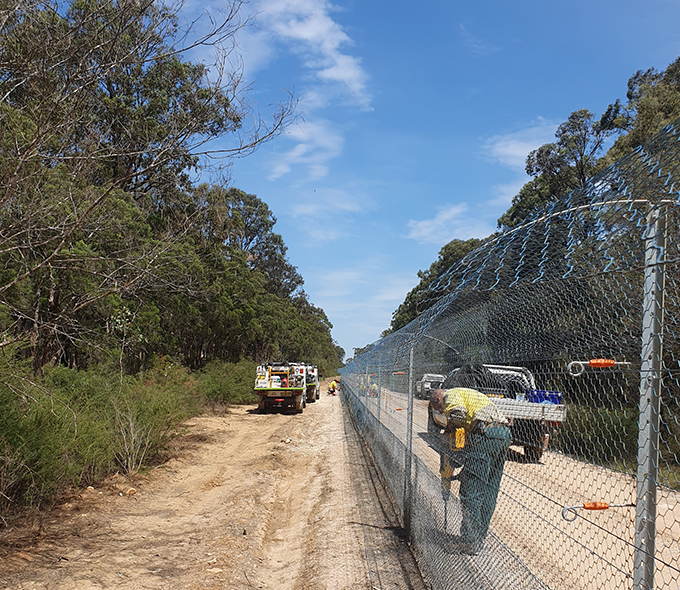 Workman fixing skirt of mesh fence to ground