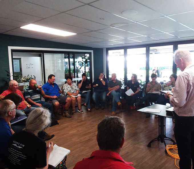 A group of individuals are seated in a semi-circle during a meeting with one person standing at the front presenting